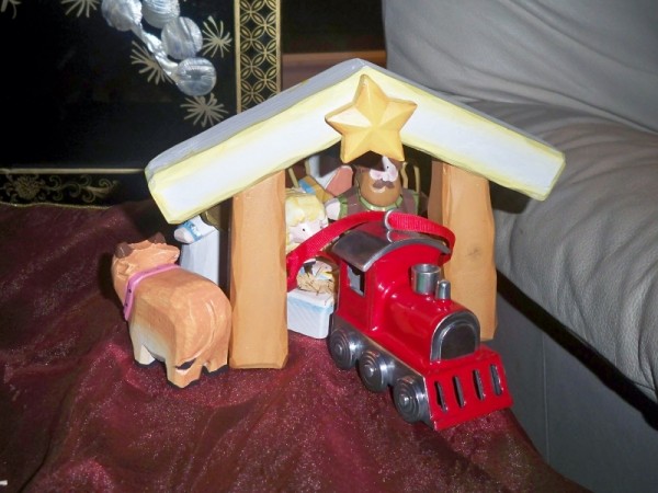 Train ornament pulling baby Jesus coach with sheep on top through manger/tunnel while all other figures following behind