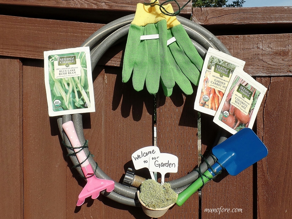 Repurposed Garden Hose Wreath - festive gardening themed wreath made from an old hose and some colorful kids gardening tools.
