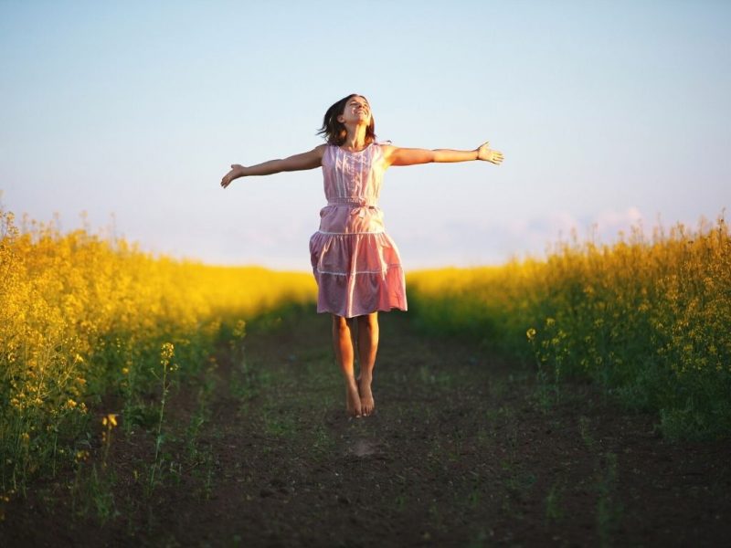 joyful woman with outstretched arms on a path in the middle of yellow wildflowers - kids with Autism need friends