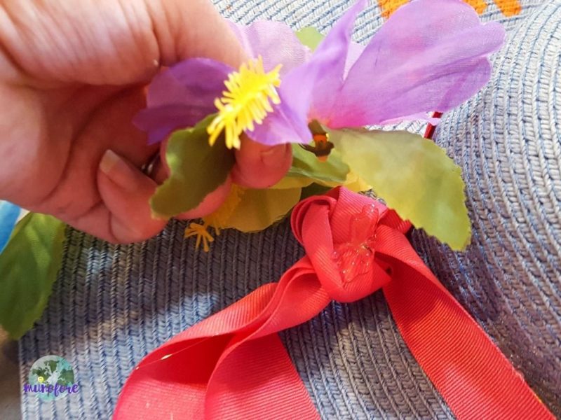 hand placing silk flower in glue on a hat